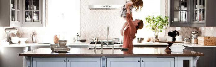 Mother and child laughing in a modern kitchen with grey window style cabinets and a large kitchen island in front of them.